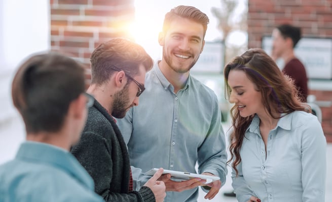 Nachhaltige Transformation erfolgreich gestalten: Mehrere Menschen in formeller Kleidung stehen zusammen und schauen auf ein Tablet.