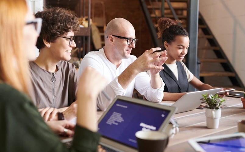 Eine Runde von vier Mitarbeitenden sitzt an einem Tisch mit Laptops und diskutiert miteinander über das Talentmanagement im Unternehmen.