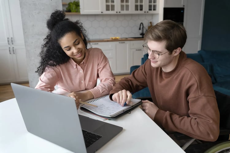 Eine Frau und ein Mann sitzen an einem Schreibtisch und schauen auf einen Block, ein Laptop steht aufgeklappt. Bernd Feix im Interview zu Inklusion.