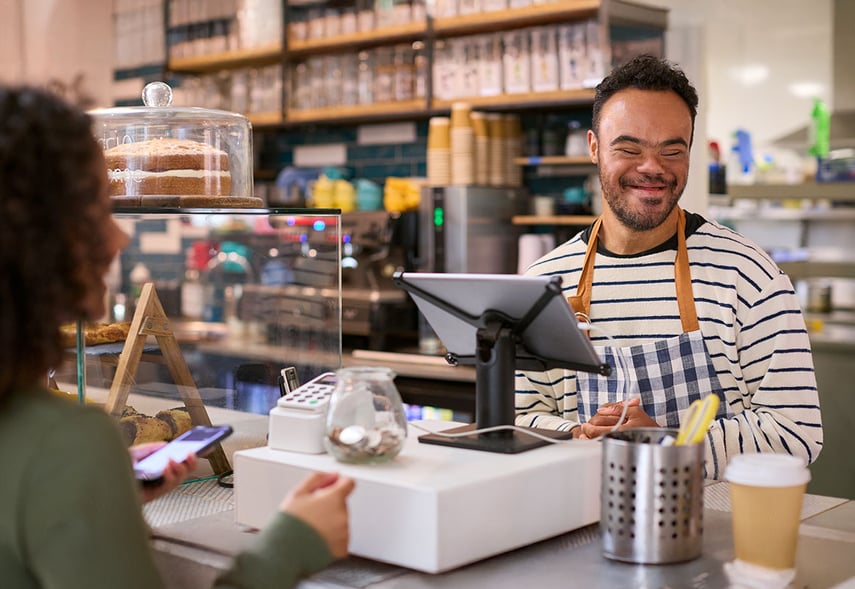 Mann mit Down-Syndrom bedient weibliche Kundin an der Kasse eines Cafés