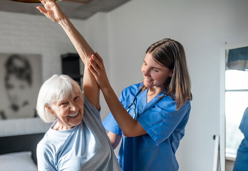 Auf dem Foto ist eine Frau die eine Übung macht und dabei einen Arm über dem Kopf streckt, eine andere Frau hilft ihr dabei  
contec conPrimo Beratungskompetenz Medizinische Versorgung­szentren als strategische Erweiterung im Sozialunternehmen