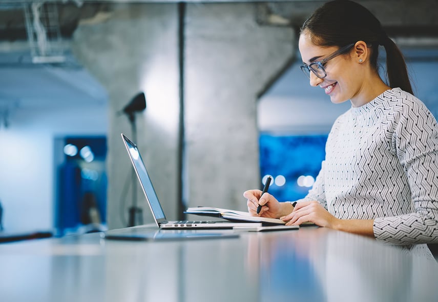 Eine Frau steht vor einem Laptop und notiert Infos zur Transformation in Sozialunternehmen