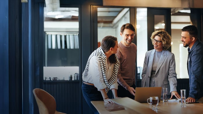 Kolleg*innen im Büro stehen um einen Tisch herum und unterhalten sich
