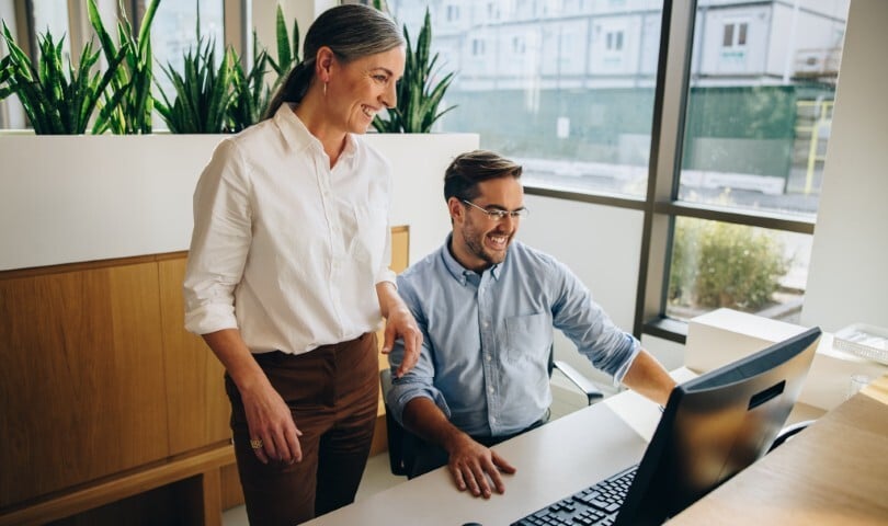 Zwei Kolleg*innen stehen vor einem Computerbildschirm und sprechen über Optionen der Versorgungsstrukturgestaltung