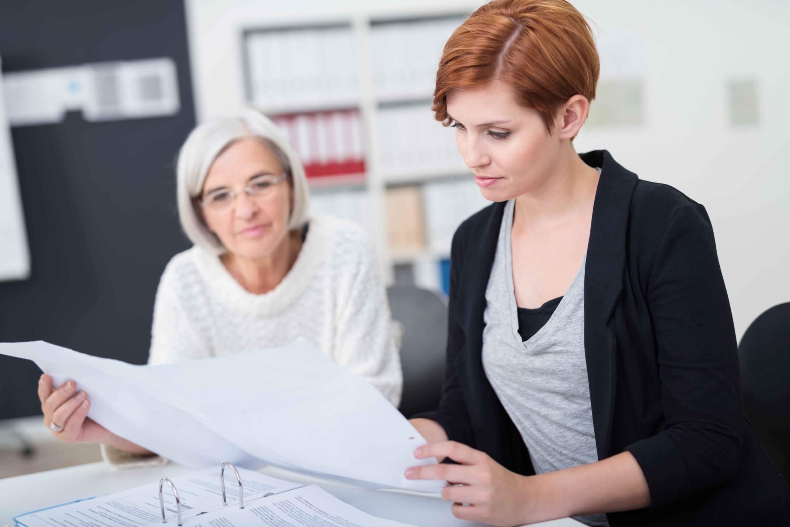 Zwei Frauen schauen sich eine indikatorengestützte Qualitätsprüfung auf einem Dokument an. 