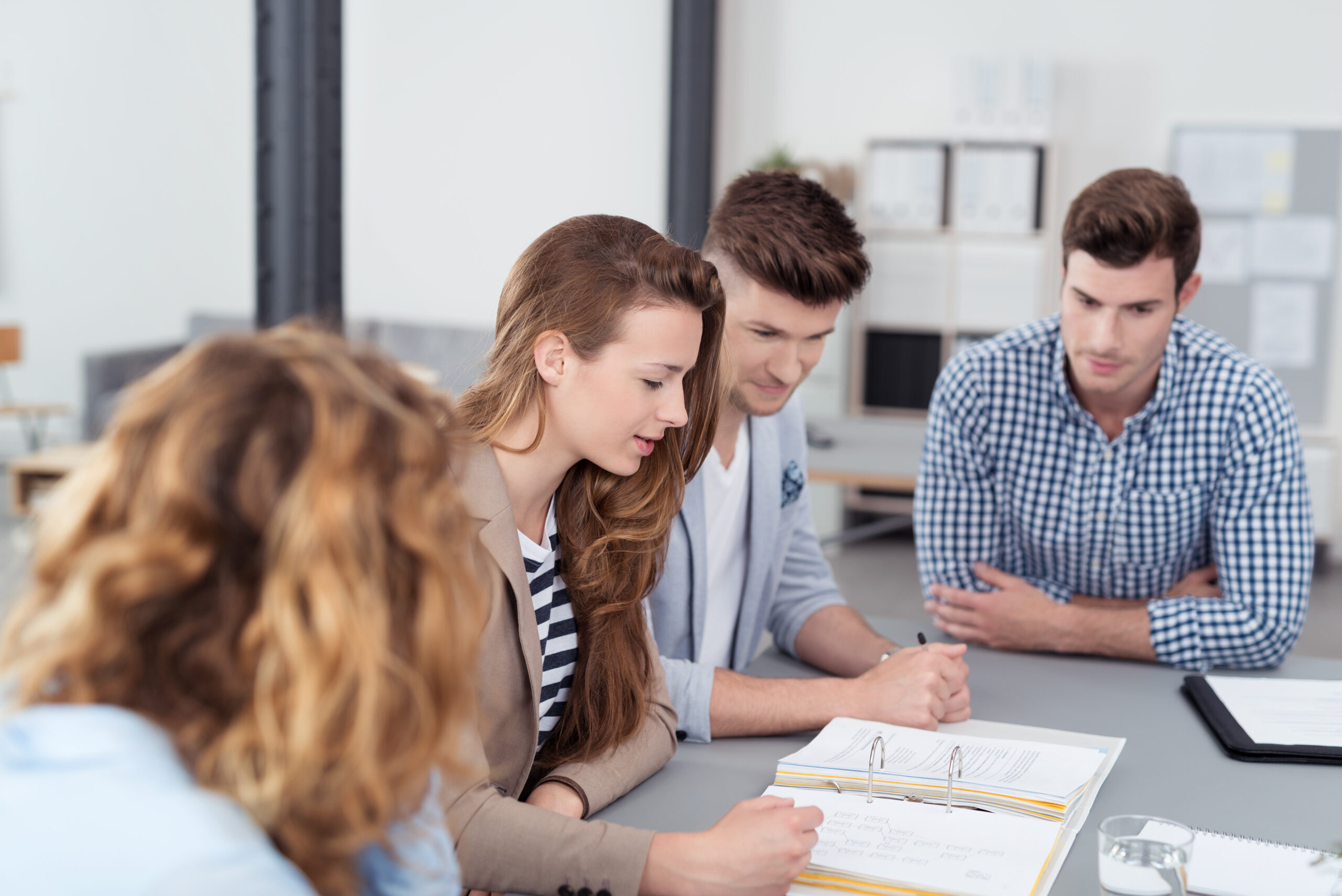 Eine Gruppe junger Büroangestellter sitzt am tisch und bespricht die Unterlagen.