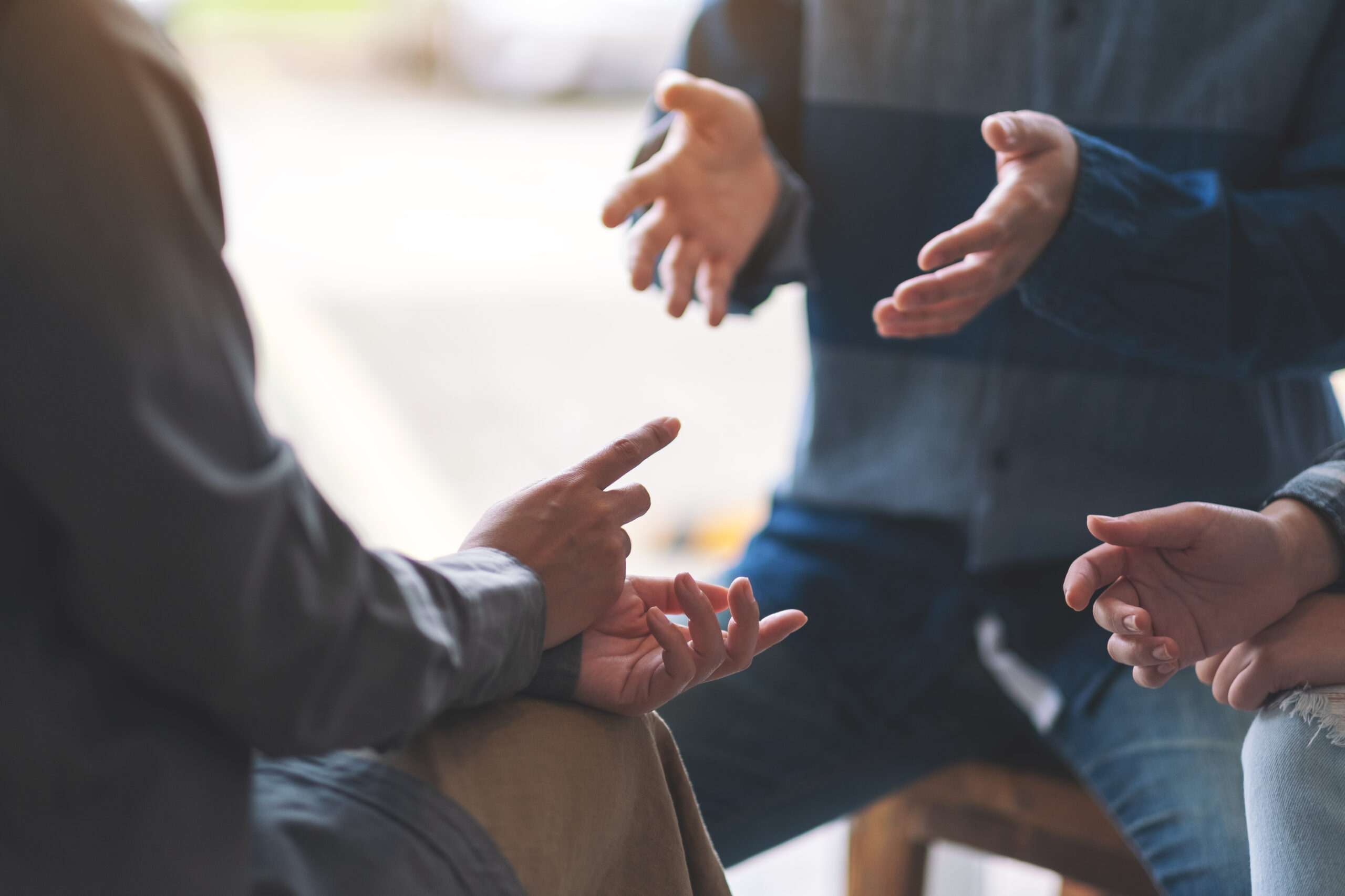 Drei Leute sitzen sich gegenüber und sprechen miteinander. Zu sehen sind die Hände und Oberkörper der Personen