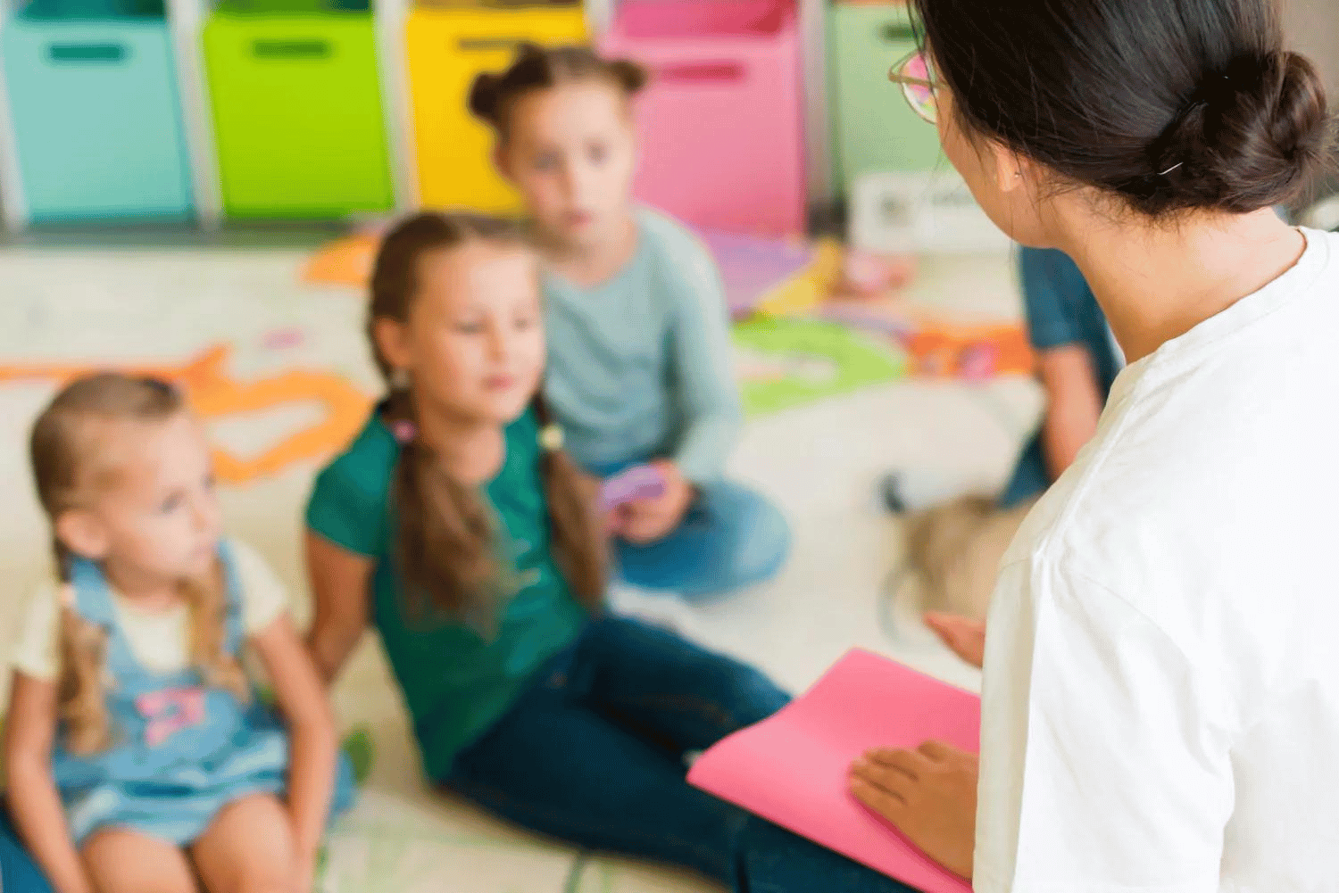 Mädchen und Jungen in einer Kindertageseinrichtung hören ihrer Erzieherin zu.