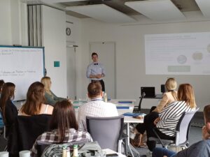 Anwendungsbeispiel World Café bei contec in Bochum, Thema Fachkräftesicherung: Attraktive Ausbilder. Auf dem Bild hält ein Experte einen Impuls zum Thema Digitalisierung. Die Teilnehmenden des World Cafés sitzen an Tischen und hören zu.