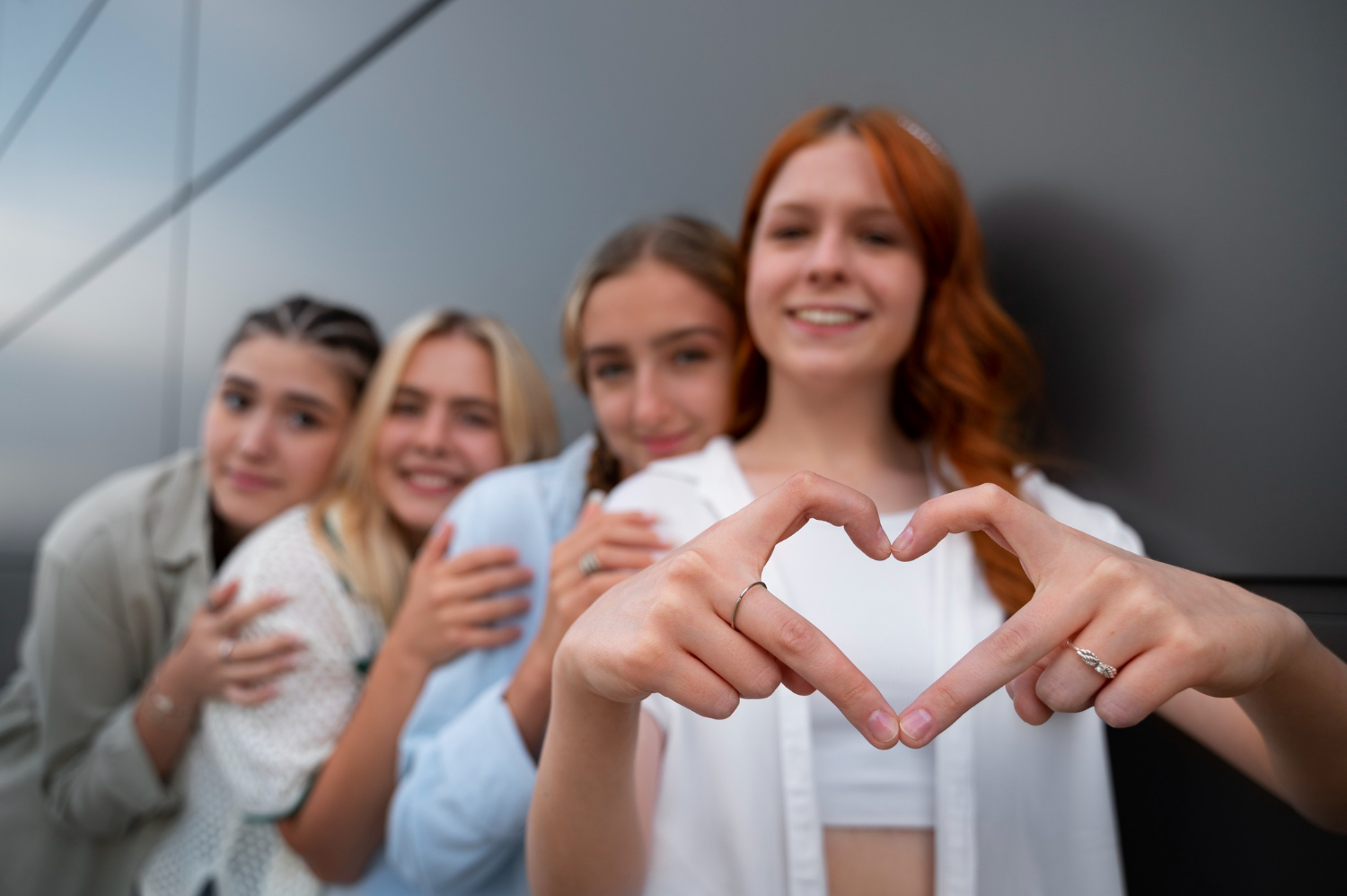Vier junge Frauen stehen hintereinander. Die vordere Frau bildet mit ihren beiden Händen ein Herz.